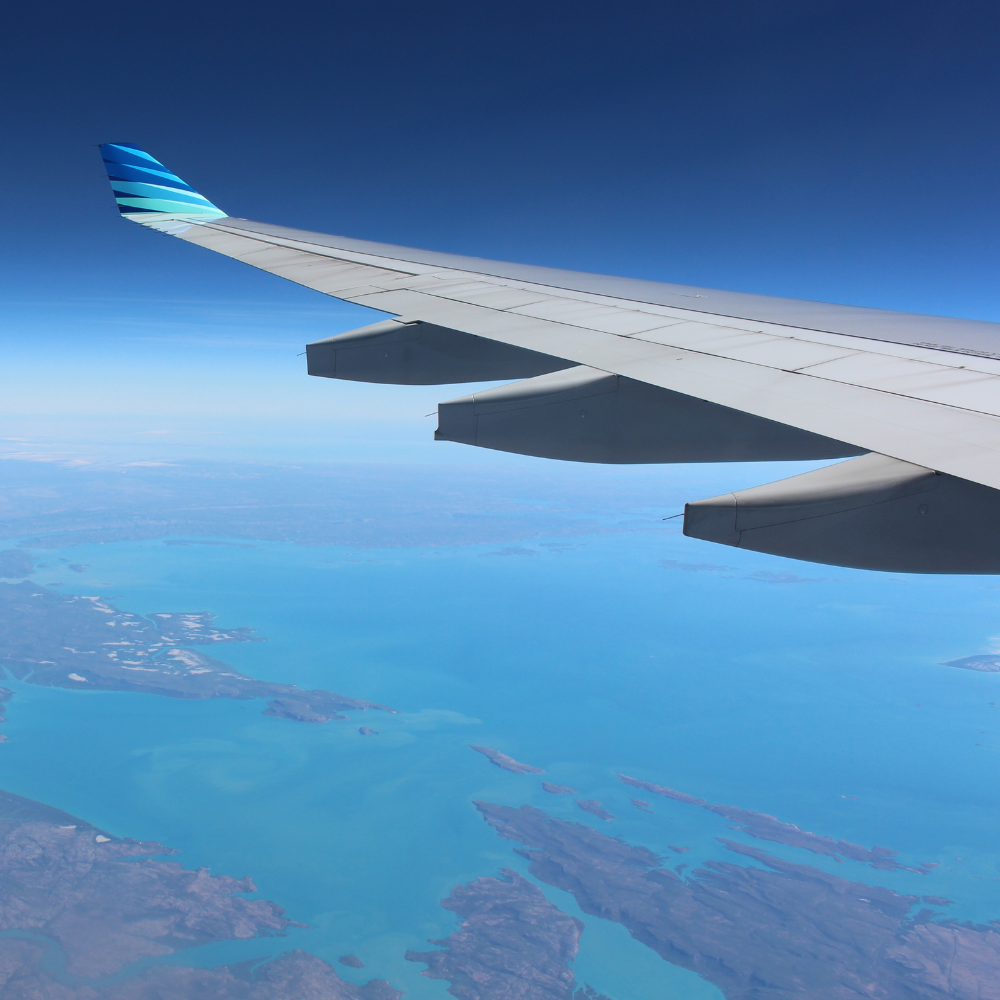 Vue spectaculaire depuis un avion sur une mer turquoise et des paysages insulaires, accentuée par l'aile de l'avion sous un ciel bleu clair.